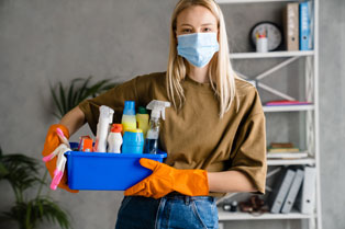 woman in face mask with cleaning supplies